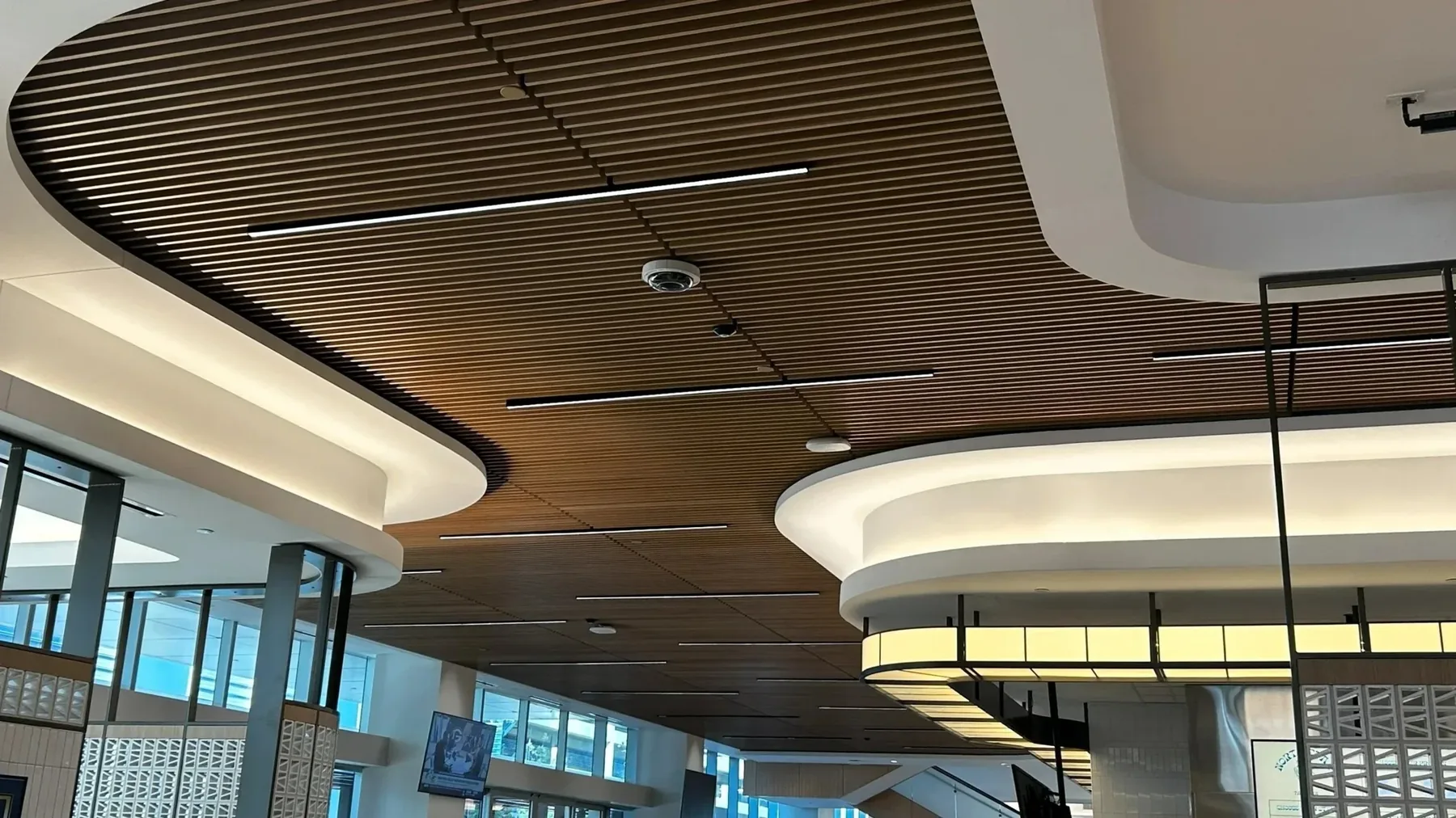 A curved slatted ceiling carrying linear light, cameras and sensors